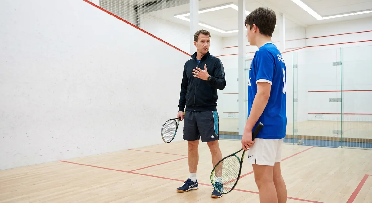 A professional squash coach demonstrating forehand technique to players on the court